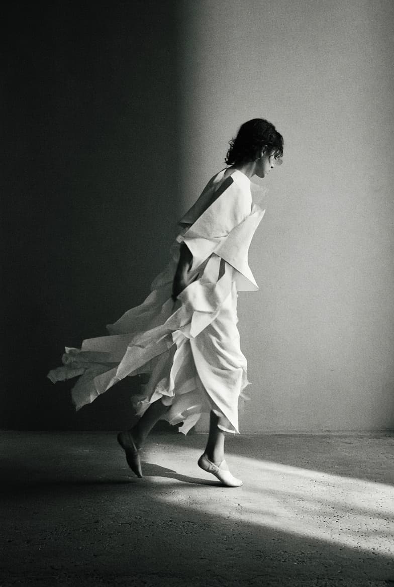 An editorial still - a paper-panelled dress caught mid-stride in one shaft of raking light