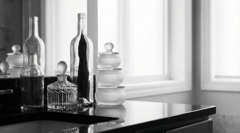 Frosted glass jars and a bottle on a dark sill against a bright window