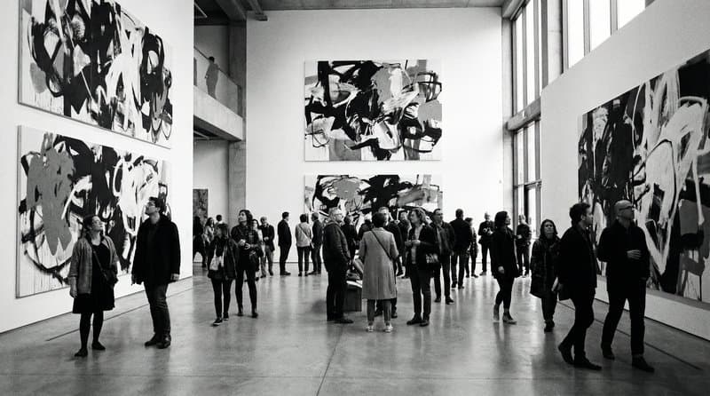 A gallery opening, visitors gathered in front of large abstract canvases
