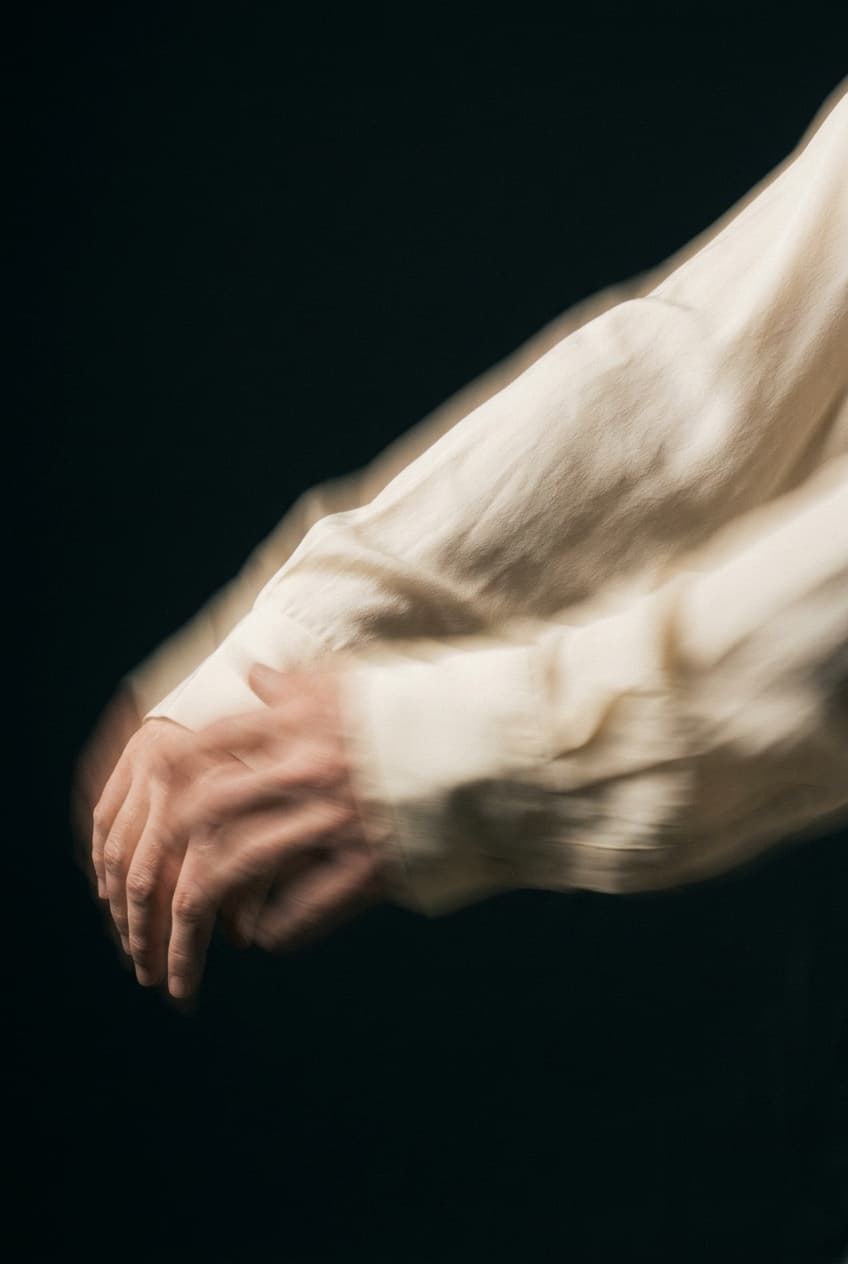 Hands holding a printed page proof of a product still life against a dark ground