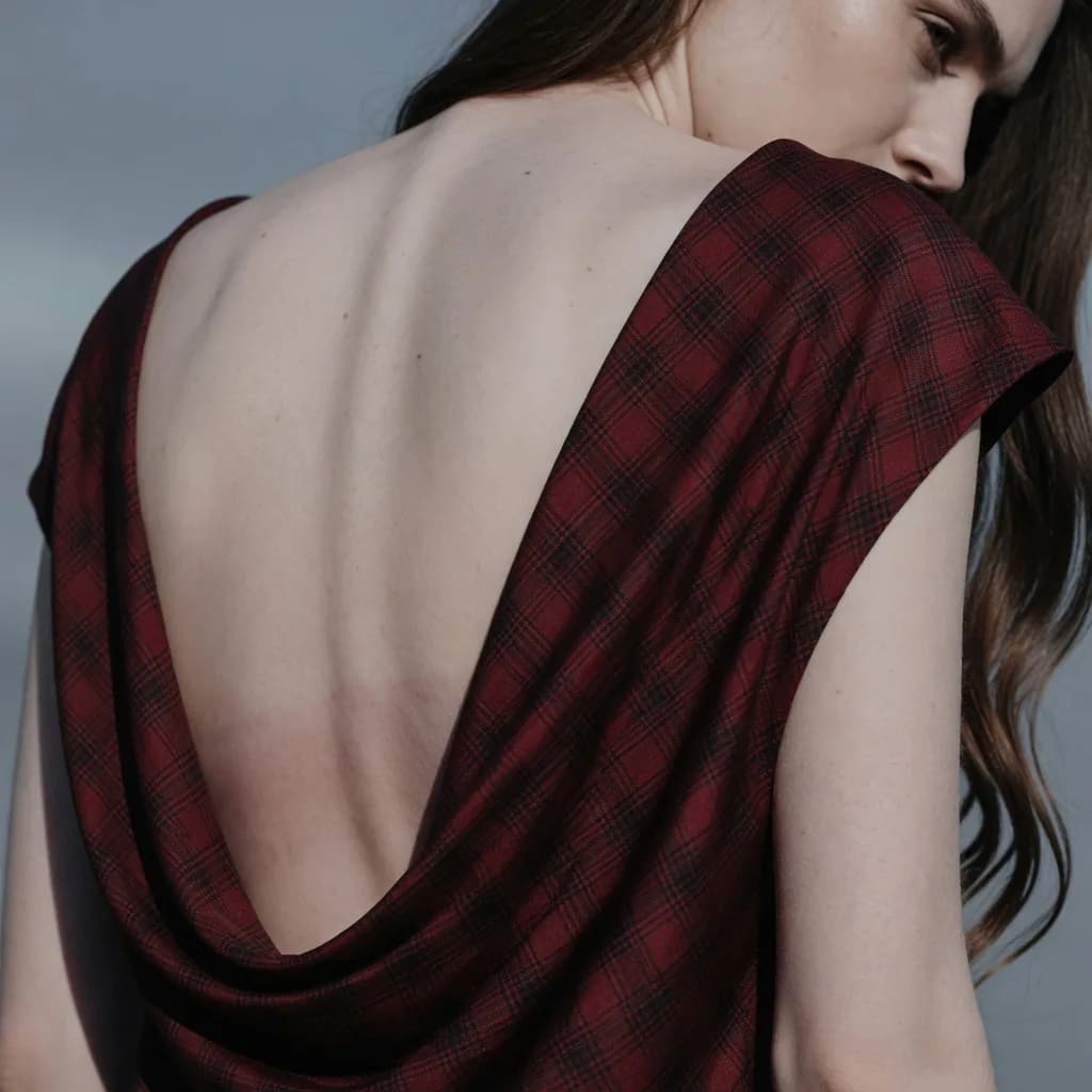 Macro detail of red and black tartan draped across a bare back, the weave and bias visible