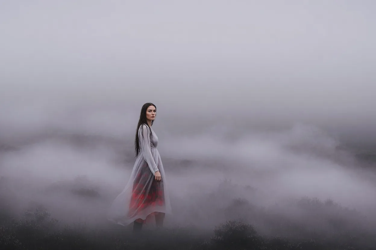 A figure in a tartan dress almost lost in dense hill fog, only the red of the skirt reading through
